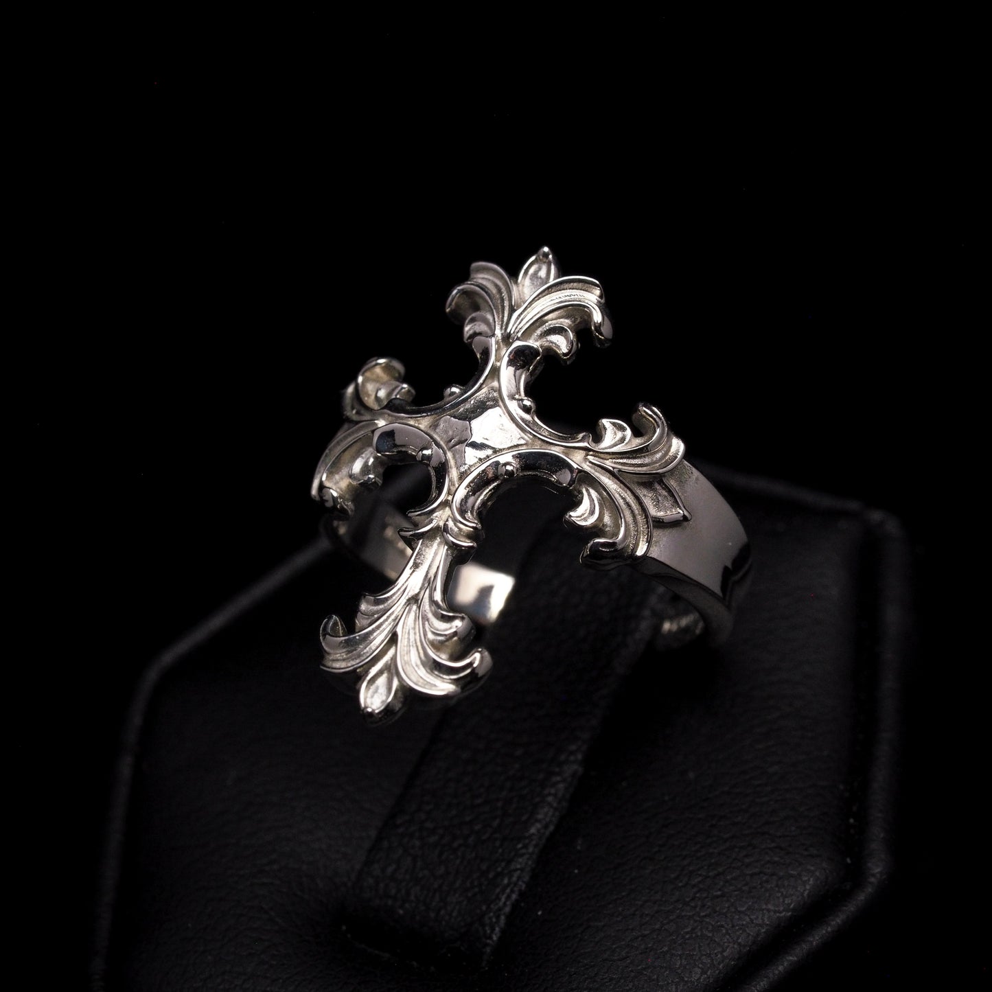 Silver cross ring on a dark cushion