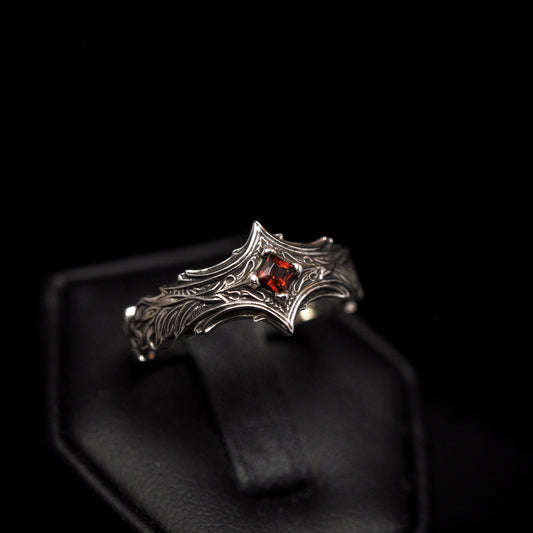 A sterling silver ring with a square, princess cut red gemstone, displayed on a black mount.