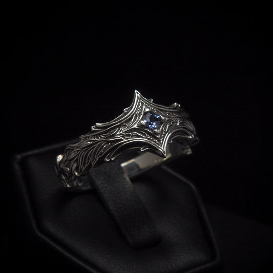 A sterling silver ring with a square, princess cut gemstone set in a flame-like design on a black band.