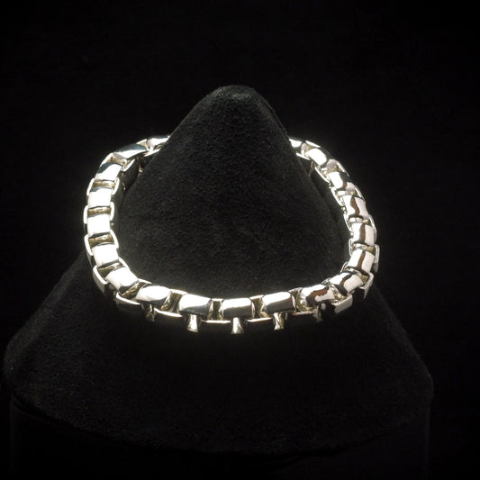 A large round box chain bracelet made of silver, displayed on a black stand.