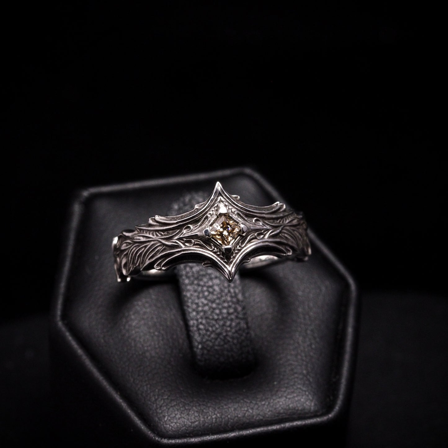 Silver ring with a central gemstone on a black stand against a black background