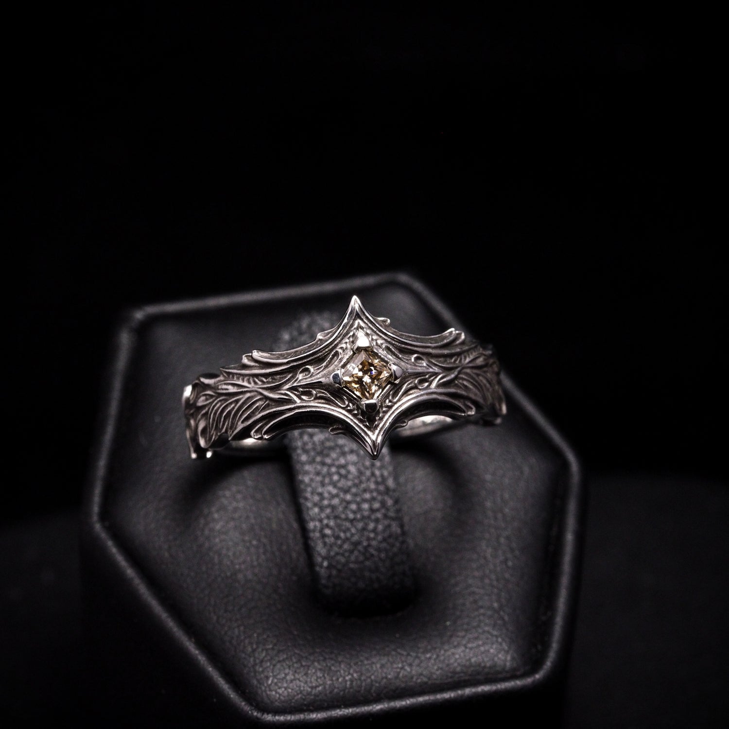 Silver ring with a central gemstone on a black stand against a black background
