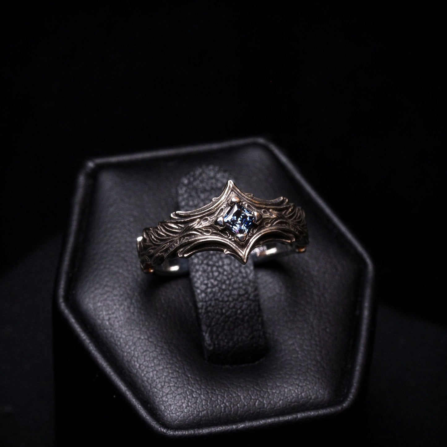 Silver ring with a blue gemstone on a black leather stand against a dark background