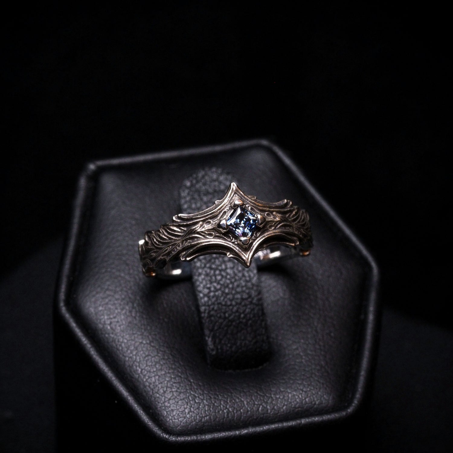 Silver ring with a blue gemstone on a black leather stand against a dark background