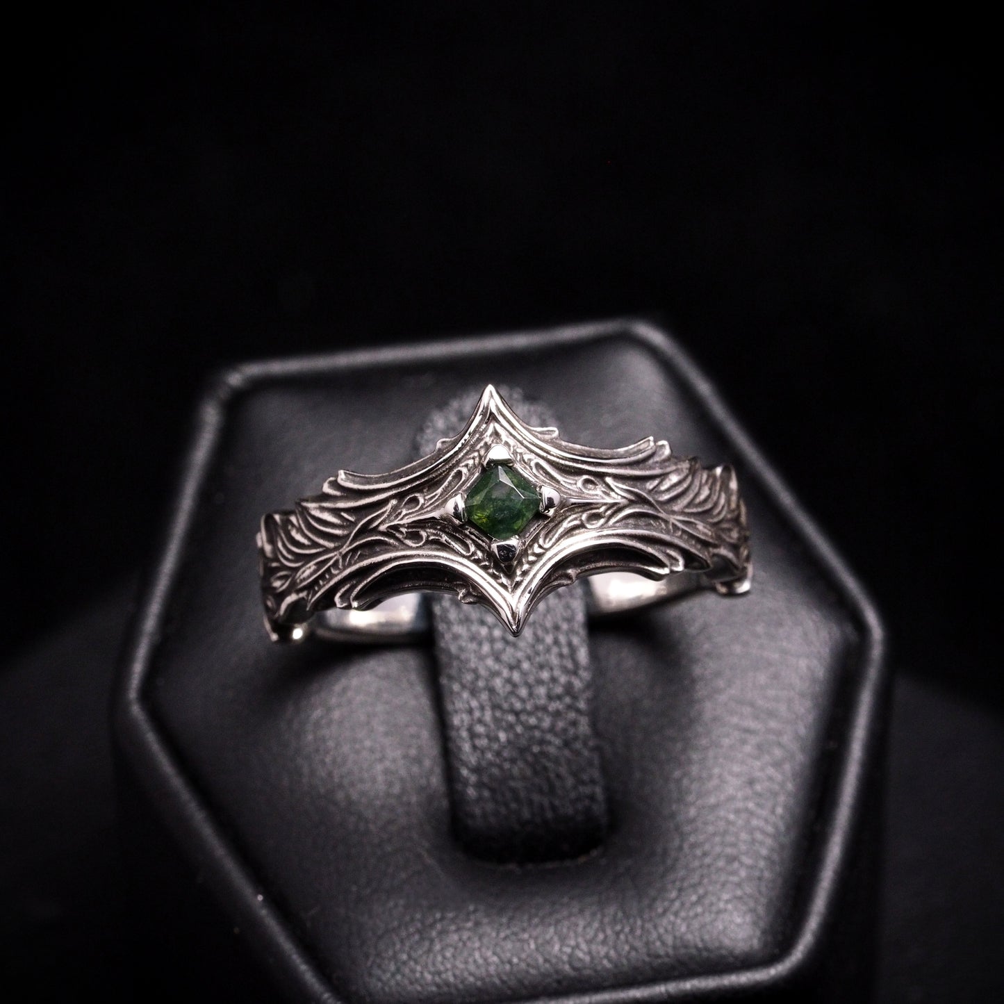 Silver ring with a mossy green gemstone on a black background