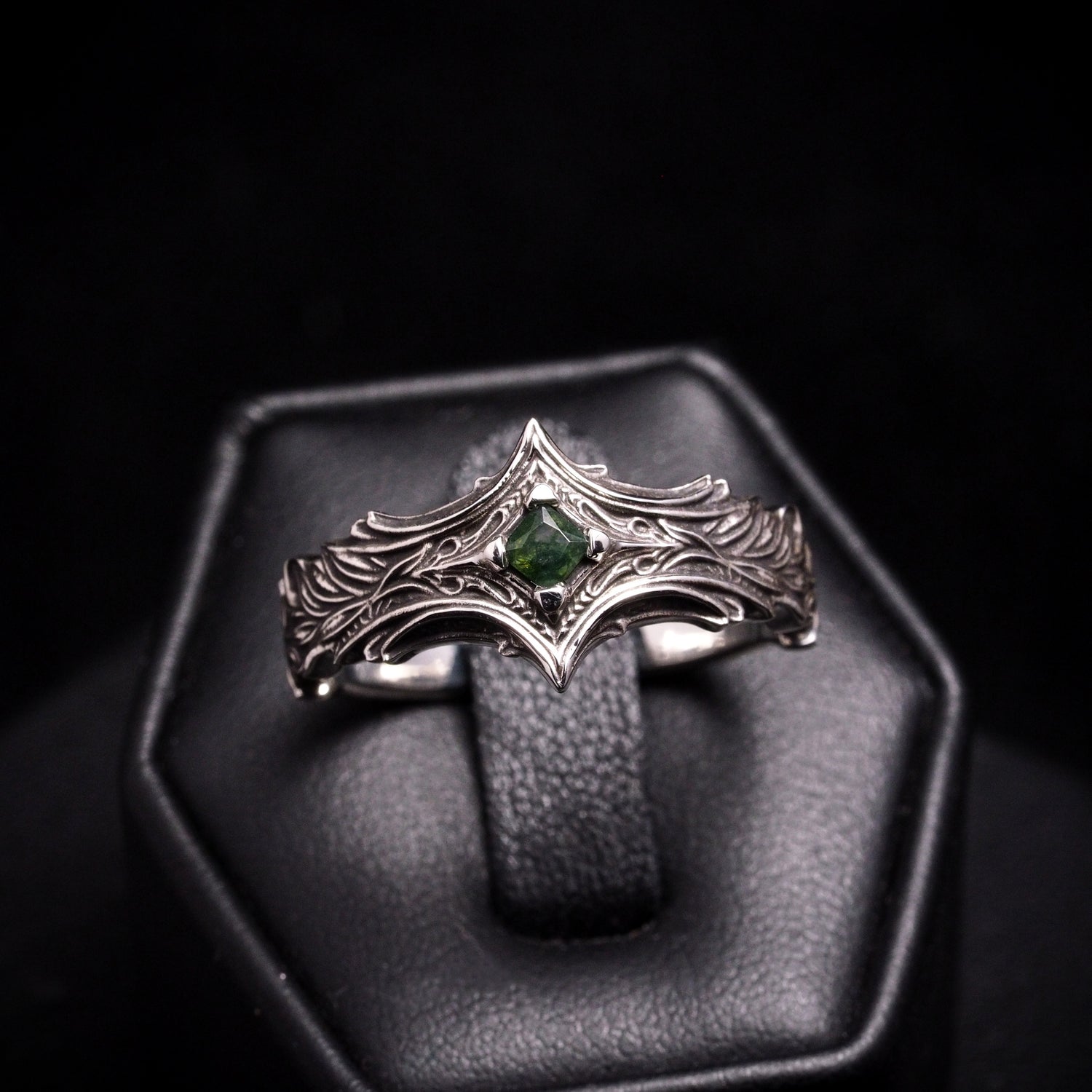 Silver ring with a mossy green gemstone on a black background