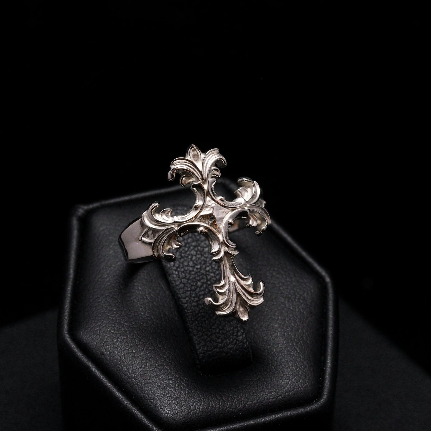 Decorative silver pendant on a black cushion against a dark background