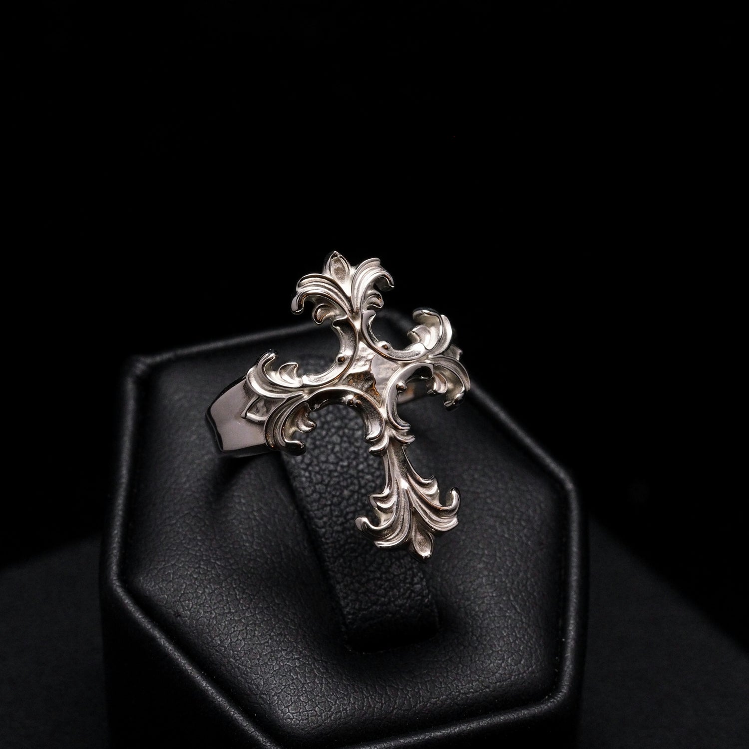 Decorative silver pendant on a black cushion against a dark background