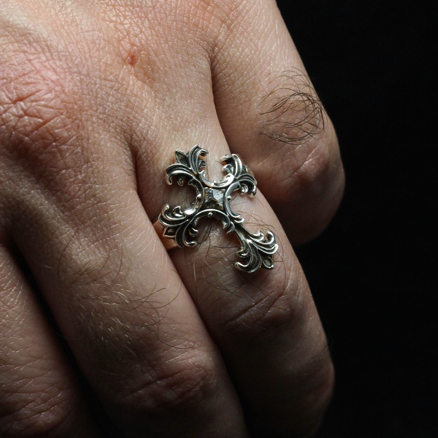 Silver ring with intricate design on a finger against a dark background