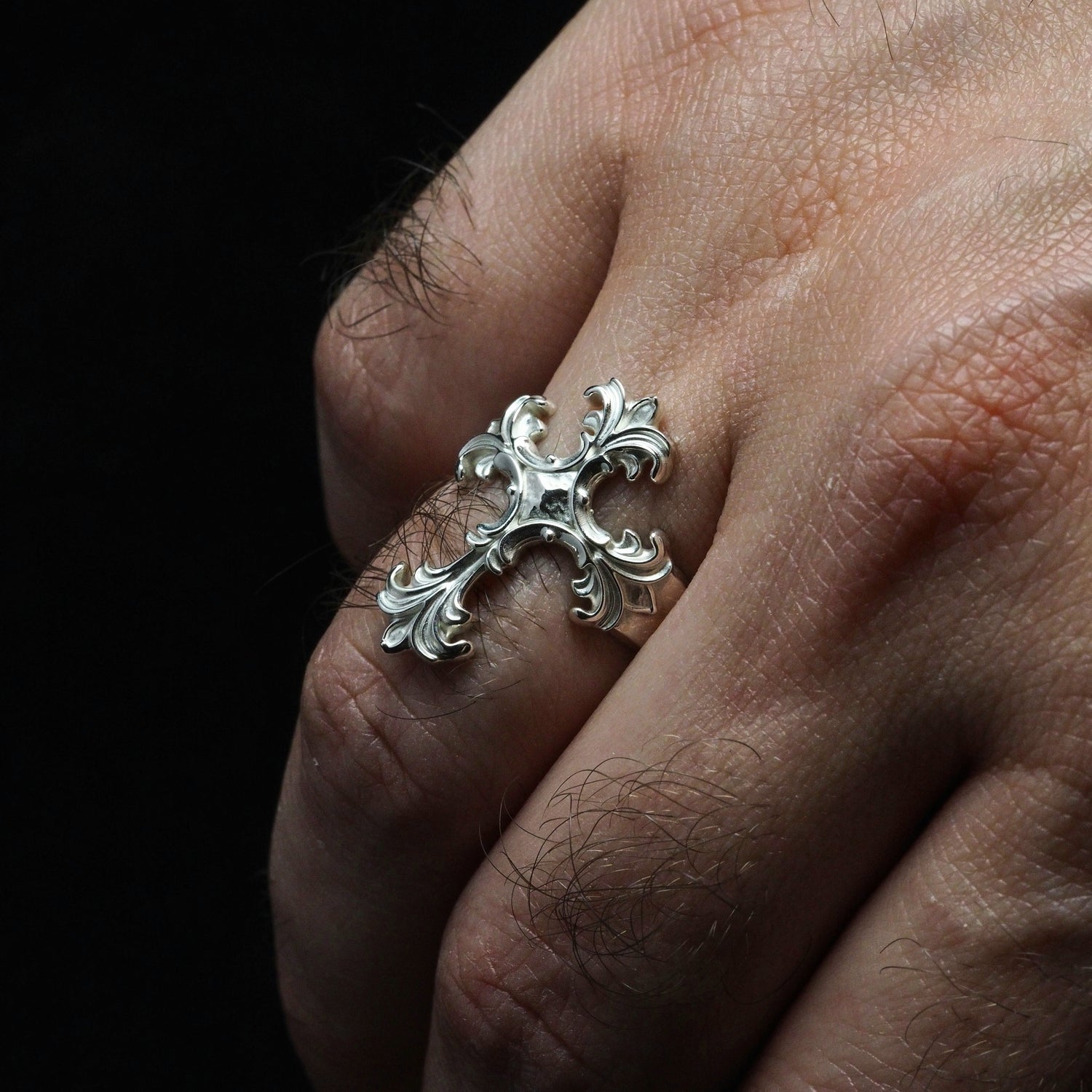 Silver ring with intricate design on a person's finger against a dark background