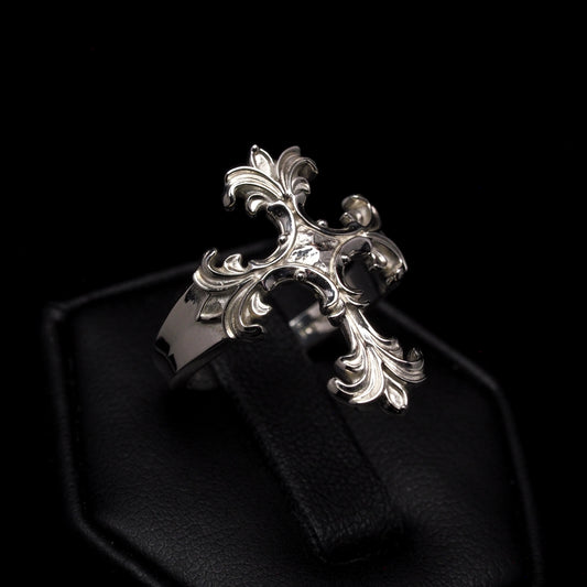An ornate silver cross ring displayed on a black cushion.
